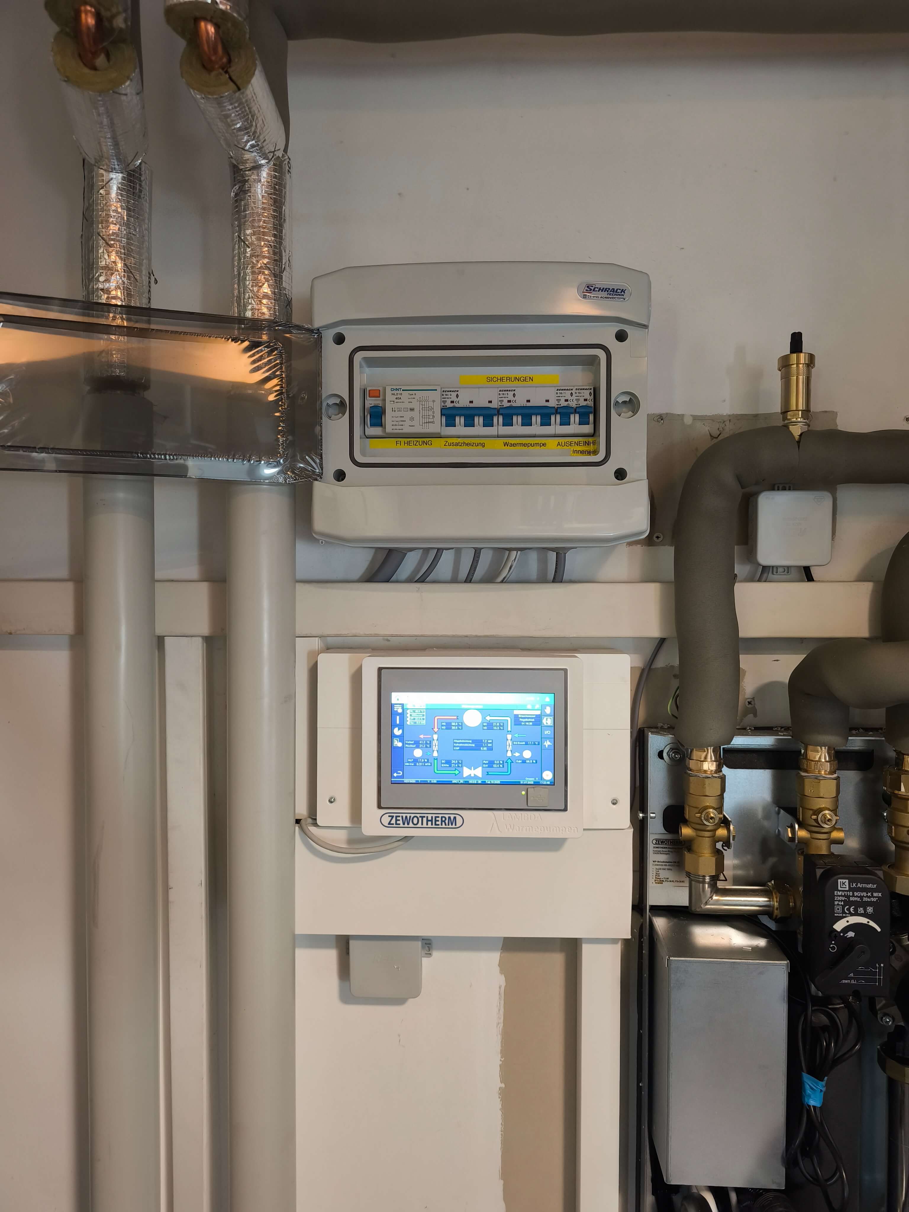 In einem Technikraum sind Heizungsrohre und ein Steuergerät für die Wärmepumpe montiert, das die Temperaturregelung anzeigt.